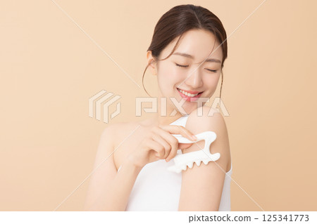 Portrait of a young woman massaging her shoulders with a gua sha 125341773