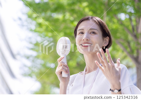 Business: A woman walking through an office district cooling off with a handheld fan 125342316