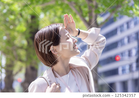 Business: A woman walking through an office district blocking the sunlight with her hand Business: A woman walking through an office district blocking the sunlight with her hand 125342357