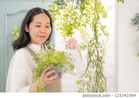 Smiling adult woman taking care of plants indoors | Florist gardening shop classroom image | Well-being girl | Well-being Smiling adult woman taking care of plants indoors | Florist gardening shop classroom image | Well-being girl | Well-being 125342364