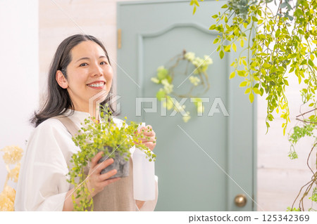 Smiling adult woman taking care of plants indoors | Florist gardening shop classroom image | Well-being girl | Well-being 125342369