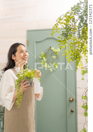 Smiling adult woman taking care of plants indoors | Florist gardening shop classroom image | Well-being girl | Well-being 125342371