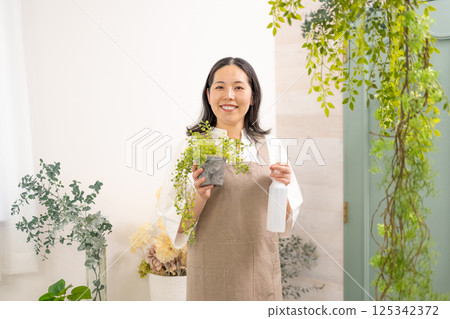 Smiling adult woman taking care of plants indoors | Florist gardening shop classroom image | Well-being girl | Well-being 125342372