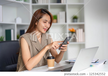 Communication and Technology. A young woman engaged in mobile communication while enjoying coffee in her organized workplace. 125342552