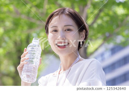 Business: A woman walking through an office district with a handheld fan 125342640