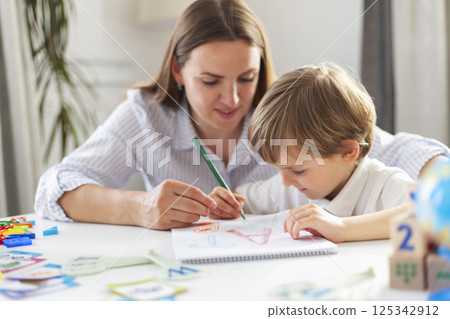 Mother teaching child to draw in homeschool setting 125342912