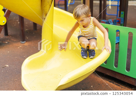 Boy crouching on yellow playground slide 125343054