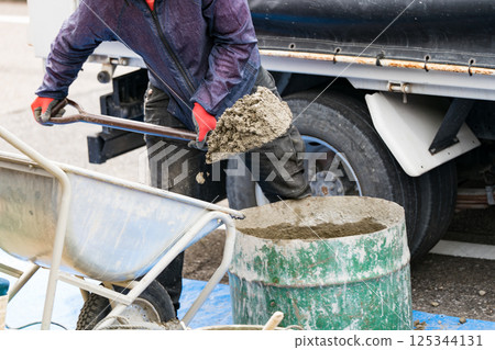 A construction worker uses a shovel to fill a drum with sand to make concrete 125344131