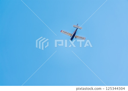 Small ultralight airplane with overhead wing and single propeller flying in sunset sky. 125344304