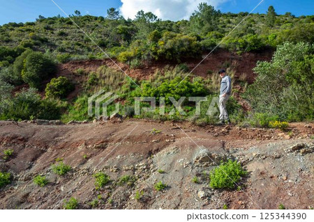 A senior man hikes wilderness trail along sedimentary rock ledge green hillside nature background 125344390