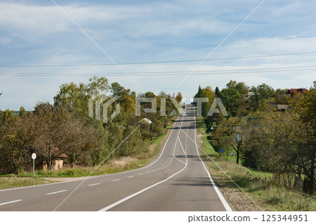 Journey through the rolling hills under a clear blue sky in late autumn showcasing a serene rural road setting 125344951