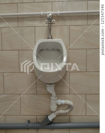 clean white urinal is mounted against beige tiled wall, showcasing contemporary plumbing. clean white urinal is mounted against beige tiled wall, showcasing contemporary plumbing. 125347340