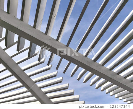 architectural lines wooden pergola contrasted against bright blue sky on sunny day. architectural lines wooden pergola contrasted against bright blue sky on sunny day. 125347344