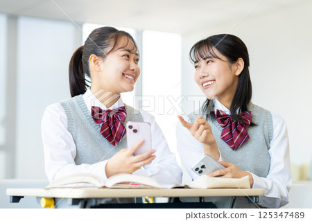 High school girls looking at their smartphones in the classroom. Photo courtesy of Denpa Gakuen, Tokyo Electronics College. 125347489