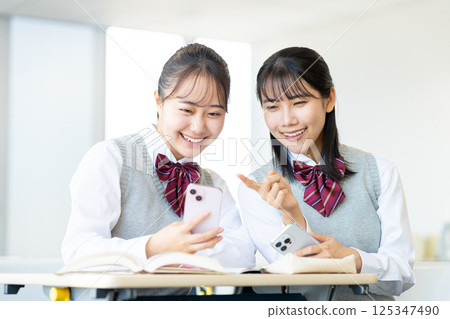 High school girls looking at their smartphones in the classroom. Photo courtesy of Denpa Gakuen, Tokyo Electronics College. 125347490