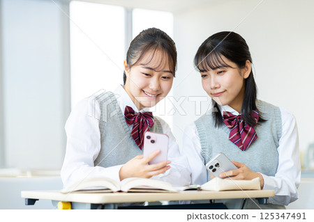High school girls looking at their smartphones in the classroom. Photo courtesy of Denpa Gakuen, Tokyo Electronics College. 125347491