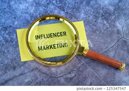 A golden magnifying glass rests on yellow paper with the text influencer marketing, emphasizing the importance of influencer strategies in modern advertising practices 125347547