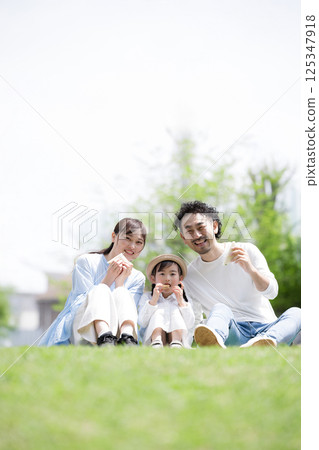 Gentle image of a family having a picnic on the lawn, looking at the camera Gentle image of a family having a picnic on the lawn, looking at the camera 125347918
