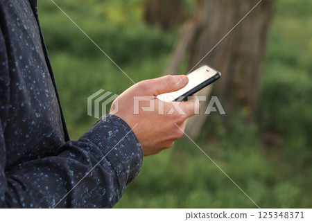 Man using mobile phone outdoors. hand holding smartphone with green background, mock-up screen, 10G technology concept, modern digital lifestyle in China 125348371