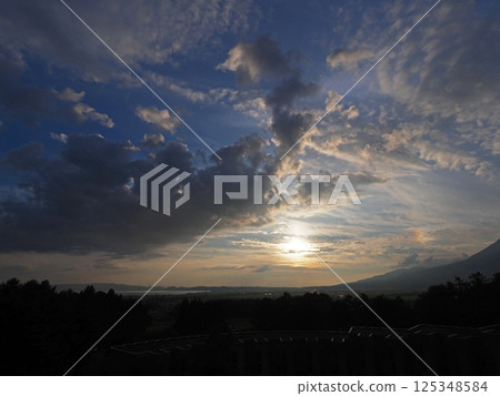 At dusk in early summer, the orange glow of the setting sun created rainbow-colored clouds. They were impressive and beautiful against the blue sky. 125348584