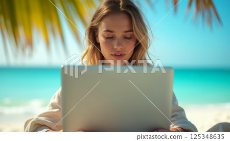 woman working on laptop on tropical beach with palm trees in background, freelance business concept 125348635