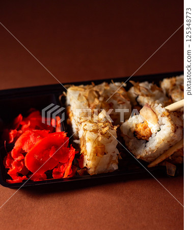 Chopsticks taking portion of sushi roll. Sushi rolls with salmon cream cheese and cucumber in take away package. Food delivery concept. Chopsticks taking portion of sushi roll. Sushi rolls with salmon cream cheese and cucumber in take away package. Food delivery concept. 125348773