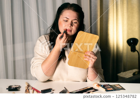 Woman looking in mirror and applying lipstick to lips. Self makeup. Preparing for event. Beauty and self-care concept 125348782