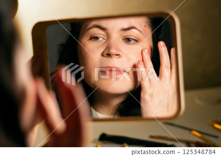 Woman applying face moisturizer cream before make-up and looking in mirror at home. Skin care concept. Self make up. 125348784