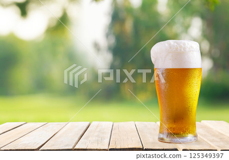 glass of beer on wooden table on green lawn background 125349397