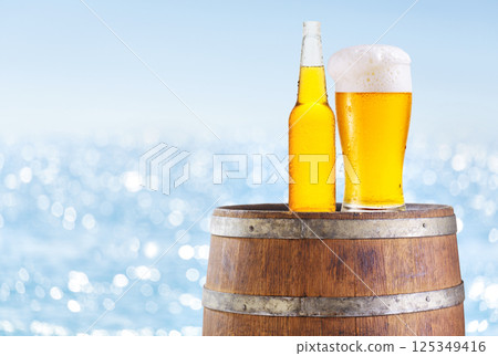 bottle and glass of beer on wooden barrel over sea background 125349416