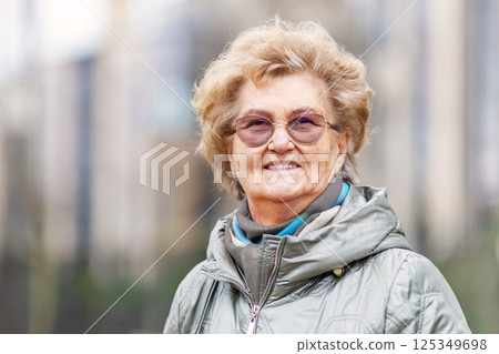 Headshot of elderly woman smiling outside in urban scene. Mature woman looks friendly wearing glasses and jacket. Longevity and active senior living concept Headshot of elderly woman smiling outside in urban scene. Mature woman looks friendly wearing glasses and jacket. Longevity and active senior living concept 125349698