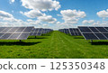 Solar panels in a green field under a bright blue sky with clouds, renewable energy concept 125350348
