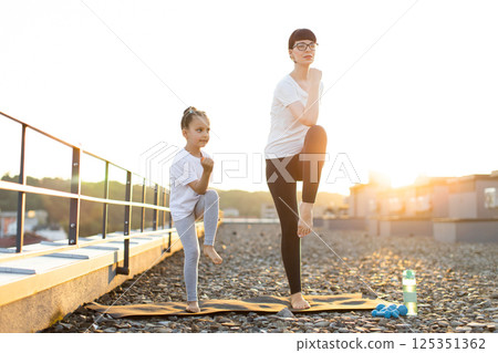 Mother and her young daughter exercising outdoors at sunrise, performing fitness stretches. Scene emphasizes family, healthy lifestyle, morning routine, physical activity, outdoor fitness Mother and her young daughter exercising outdoors at sunrise, performing fitness stretches. Scene emphasizes family, healthy lifestyle, morning routine, physical activity, outdoor fitness 125351362