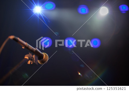 Microphone against blue stage lights. Beams from concert spotlights illuminate the microphone. Microphone against blue stage lights. Beams from concert spotlights illuminate the microphone. 125351621