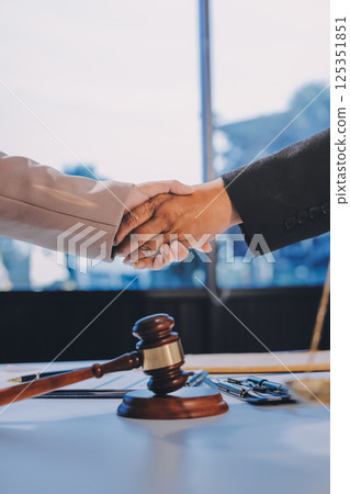 Two businesspeople are shaking hands in a law office with a scale and a gavel on the table Two businesspeople are shaking hands in a law office with a scale and a gavel on the table 125351851