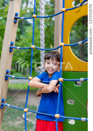 Smiling child posing on climbing net at playground Smiling child posing on climbing net at playground 125352070
