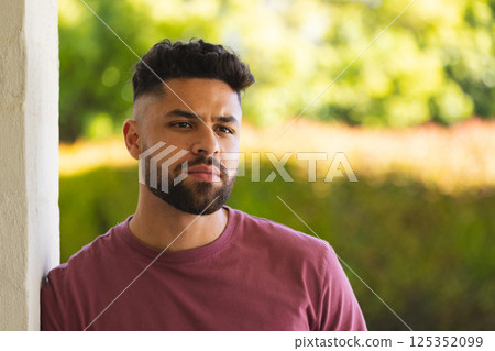 Young man outdoors leaning against wall, looking thoughtful in sunny garden Young man outdoors leaning against wall, looking thoughtful in sunny garden 125352099