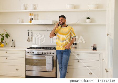 Smiling man in kitchen talking on smartphone, leaning against counter Smiling man in kitchen talking on smartphone, leaning against counter 125352136