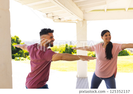 Smiling couple practicing yoga together on sunny porch, enjoying outdoor exercise 125352137