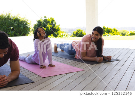 Family enjoying outdoor yoga session on mats, smiling and stretching together 125352146