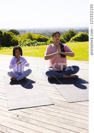 Mother and daughter practicing yoga on mats outdoors, enjoying peaceful morning Mother and daughter practicing yoga on mats outdoors, enjoying peaceful morning 125352150