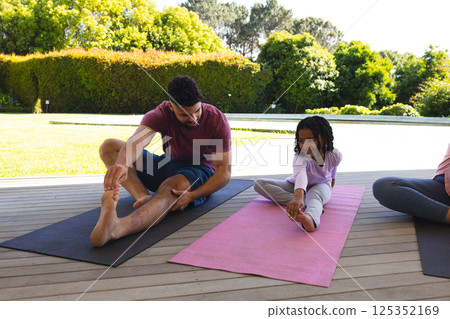 Father and daughter practicing yoga together on mats in sunny backyard Father and daughter practicing yoga together on mats in sunny backyard 125352169