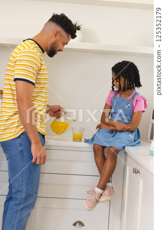 Pouring orange juice, father and daughter smiling together in kitchen 125352179