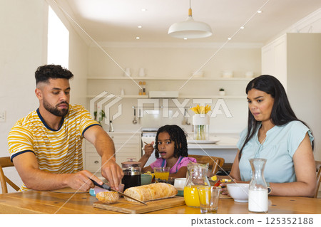 Family enjoying breakfast together at home, father slicing bread, daughter watching 125352188