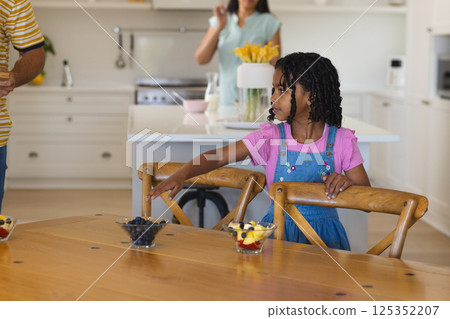 African American girl reaching for fruit bowl in kitchen while family prepares meal African American girl reaching for fruit bowl in kitchen while family prepares meal 125352207