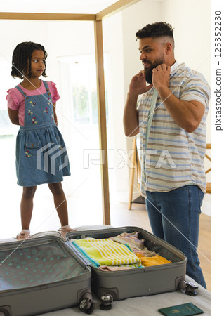 Father packing suitcase while daughter stands on bed, preparing for family trip Father packing suitcase while daughter stands on bed, preparing for family trip 125352230