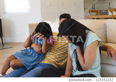 Family sitting on couch, African American girl covering ears, parents comforting her Family sitting on couch, African American girl covering ears, parents comforting her 125352232