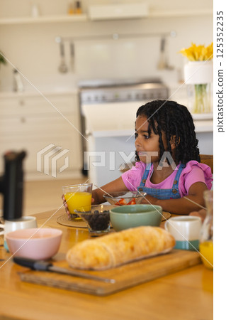 Young girl enjoying breakfast with orange juice and fruit at kitchen table, copy space Young girl enjoying breakfast with orange juice and fruit at kitchen table, copy space 125352235