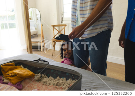 Child hugging parent while packing suitcase at home, smiling with joy 125352260