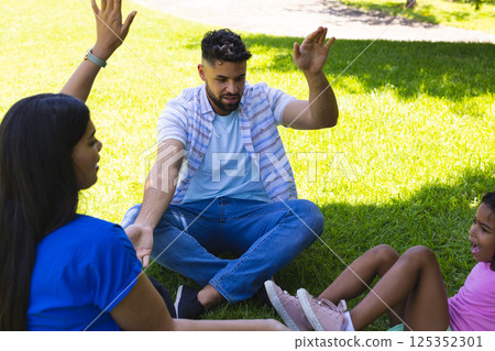 Father and daughters playing hand game on grass in sunny park 125352301